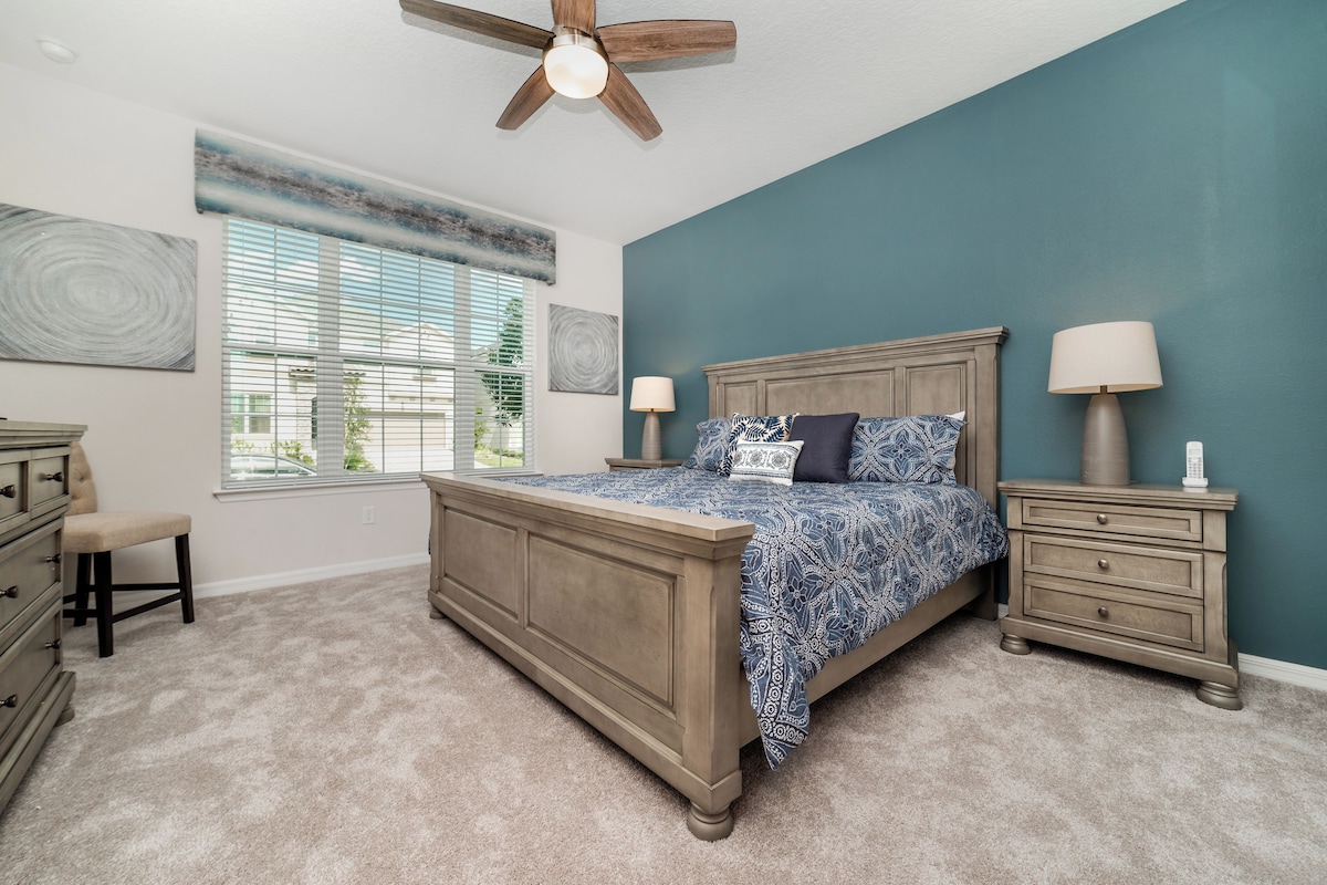 A bedroom with a bed, nightstands, a dresser, a chair, a ceiling fan, and a window with blinds.