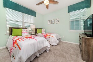 A bedroom with two beds, a ceiling fan, a dresser, and a TV.