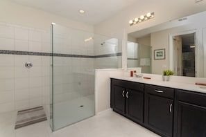 A modern bathroom with a glass shower enclosure, a large mirror, and dark cabinetry.