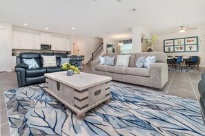 A modern living room with a black leather sofa, a grey sofa, and a wooden coffee table. There is a kitchen area with white cabinets and a microwave. - Solara Resort Homes and Townhomes (Kissimmee)