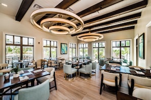 A spacious dining area with multiple tables and chairs, large windows, and a modern ceiling design.