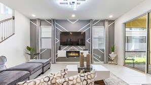 A modern living room with a fireplace, grey and white decor, and a glass door leading outside.