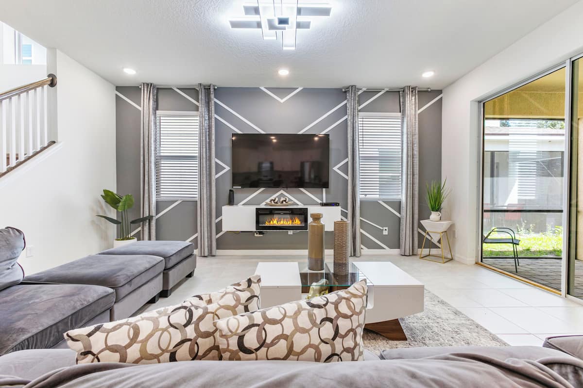 A modern living room with a fireplace, grey and white decor, and a glass door leading outside.
