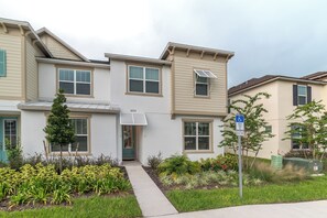 A multi-story residential building with a front entrance, a small tree, and a wheelchair-accessible sign.