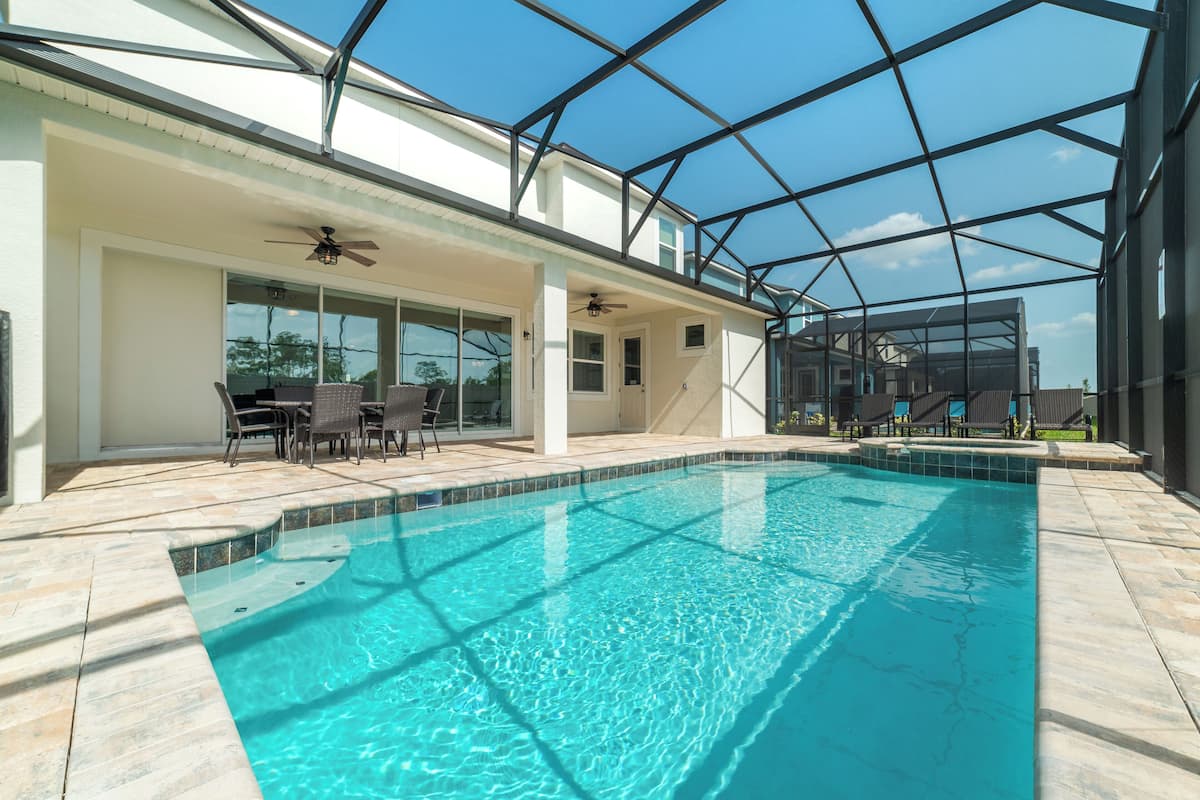 An indoor swimming pool with a glass ceiling, a ceiling fan, and a patio area with chairs and a table.