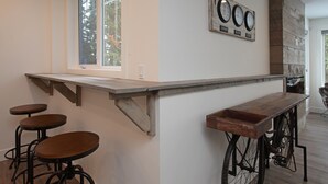 A kitchen with a wooden bar counter, three stools, and a window.