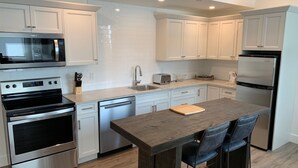 A modern kitchen with stainless steel appliances, white cabinetry, and a wooden bar area.