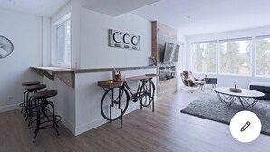A modern kitchen with a bicycle bar, wooden stools, and a large window.