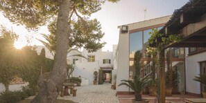 A courtyard with a cobblestone path, potted plants, and a building with large windows and a balcony. - Coliving AdD LiVitum (Ciutadella de Menorca)