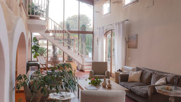 A spacious living area with a staircase leading to an upper level, a sofa, a coffee table, and various plants. - Coliving AdD LiVitum (Ciutadella de Menorca)