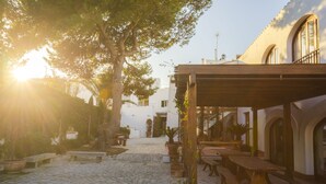 A cobblestone courtyard with outdoor seating, a pergola, and a white building with arches. - Coliving AdD LiVitum (Ciutadella de Menorca)