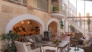 A spacious living area with a high ceiling, stone walls, and a balcony with a railing. There is a seating area with sofas and a coffee table, and a television in the background. - Coliving AdD LiVitum (Ciutadella de Menorca)