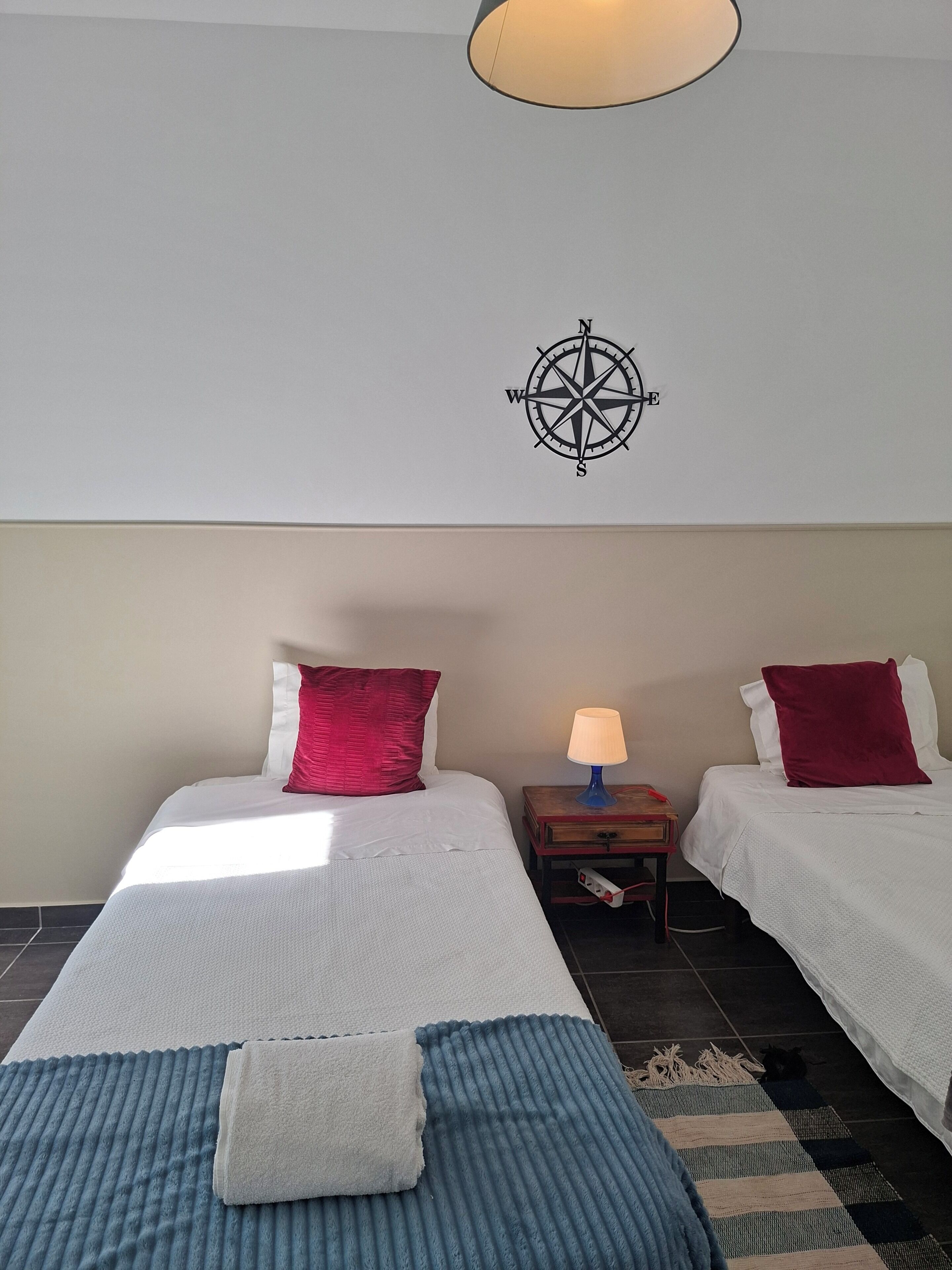 A hotel room with two beds, a wall compass, a lamp, and a rug.