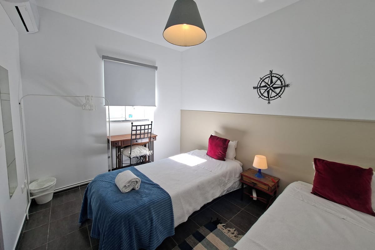 A bedroom with a bed, a desk, a chair, a nightstand, a lamp, a window, and a compass wall decoration.
