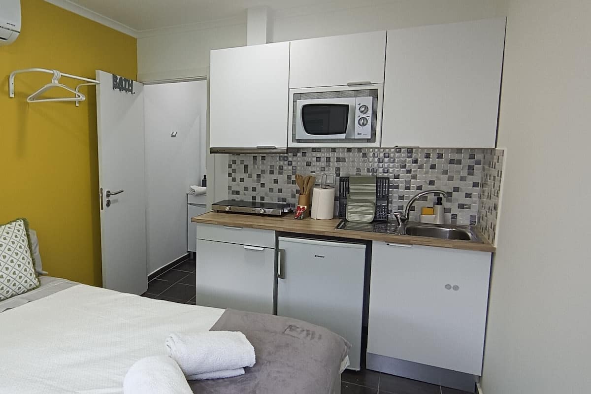 A compact hotel room with a bed, a small kitchenette, a microwave, and a compact refrigerator.