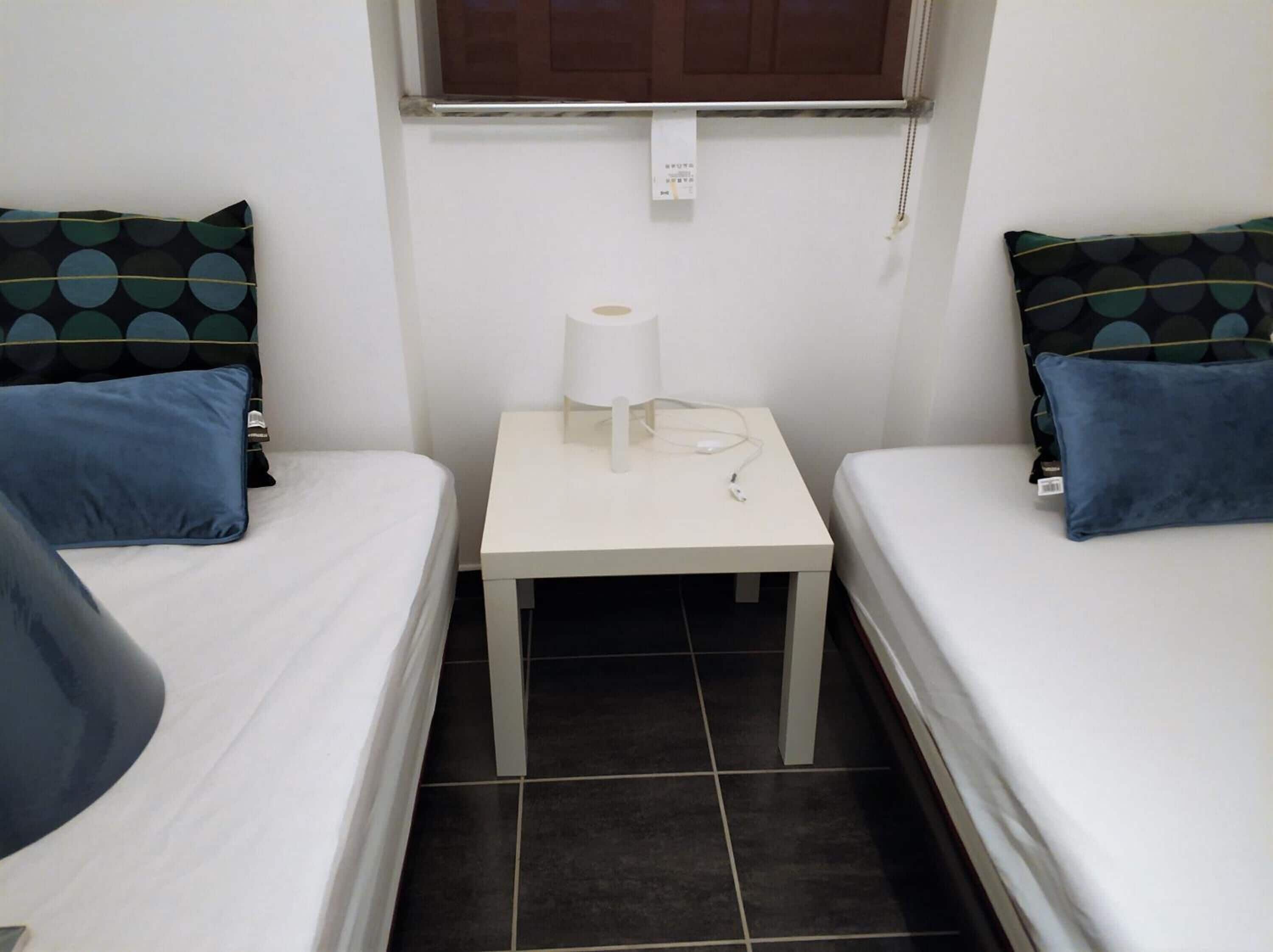 Une petite pièce avec deux lits, une table de chevet avec une lampe et une fenêtre.