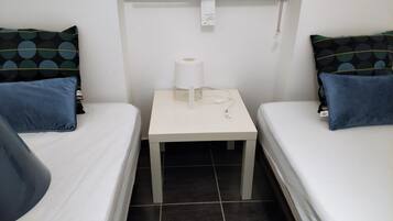Une petite pièce avec deux lits, une table de chevet avec une lampe et une fenêtre.