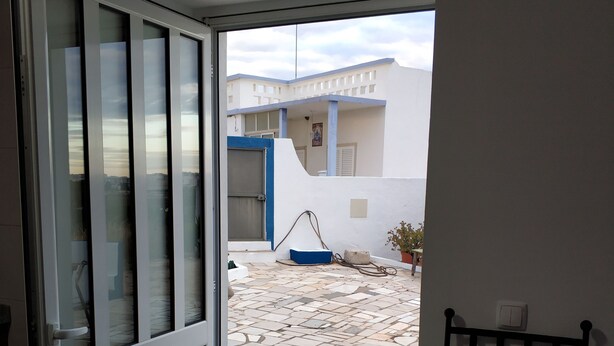 A view from a room with a door leading to a courtyard with a blue door, a potted plant, and a bench. - Sleep & Go Faro Airport Guest House (Faro)