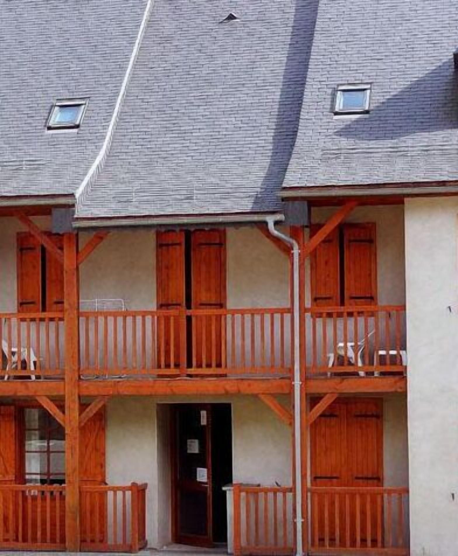 A building with a grey roof, wooden balconies, and a beige facade.