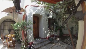 Un patio con puerta de madera, plantas en macetas y una escalera que conduce a un nivel superior.