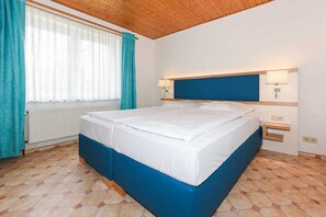 Un dormitorio con una cama, una ventana con cortinas, un radiador y un techo de madera.