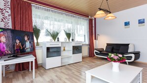 Una sala de estar moderna con televisión, muebles blancos, una mesa de comedor y un sofá.