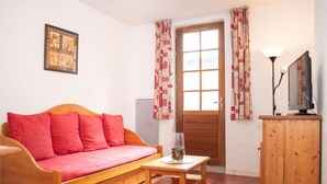 Ein gemütliches Zimmer mit einer Holzsofa, einem kleinen Holztisch, einem Schrank und einem Fenster mit Vorhängen.