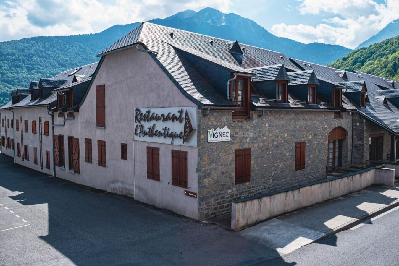 A building with a sign for 'Restaurant L'Authentique' and a 'VIGNEC' sign, surrounded by mountains.