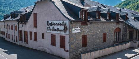 A building with a sign for 'Restaurant L'Authentique' and a 'VIGNEC' sign, surrounded by mountains.