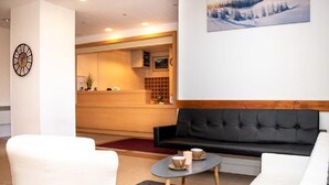 A modern hotel lobby with a reception desk, a black sofa, a white armchair, and a small table with cups. - Wifi, 1st floor, view mountain, swimming pool, balcony, parking, tv, ski locker, 35m² (Puy-Saint-Vincent)