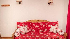 A wooden sofa with red and white patterned cushions, two wall-mounted lamps, and a wooden panel on the wall. - Wifi, 1st floor, view mountain, swimming pool, balcony, parking, tv, ski locker, 35m² (Puy-Saint-Vincent)