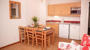 A compact kitchen with wooden cabinets, a microwave, a dishwasher, and a dining table with chairs. - Wifi, 1st floor, view mountain, swimming pool, balcony, parking, tv, ski locker, 35m² (Puy-Saint-Vincent)