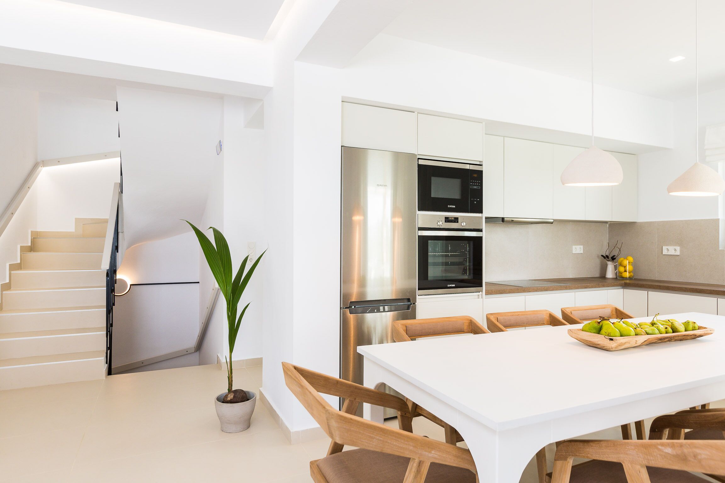 Une cuisine moderne avec des meubles blancs, des appareils en acier inoxydable et un coin repas comprenant une table blanche et des chaises en bois.