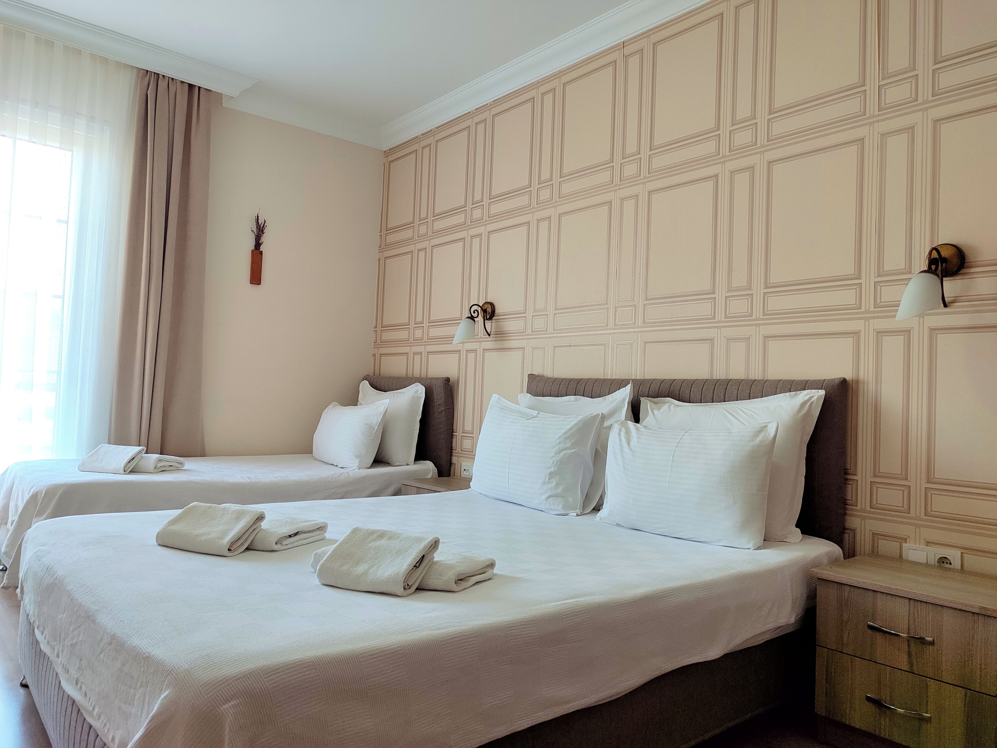 Habitación de hotel con dos camas, una mesita de noche, una lámpara y una pared con un diseño geométrico.