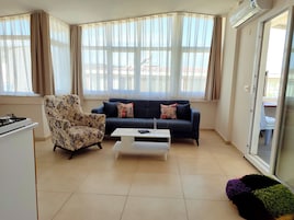 Uma sala de estar com sofá, poltrona, mesa de centro e janela com cortinas.