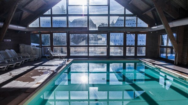 Een binnenzwembad met heldere glazen panelen en uitzicht op besneeuwde bergen door grote ramen.
