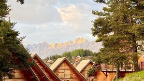 Een rij houten chalets met puntige daken, een onverhard pad ernaartoe en een berg op de achtergrond.