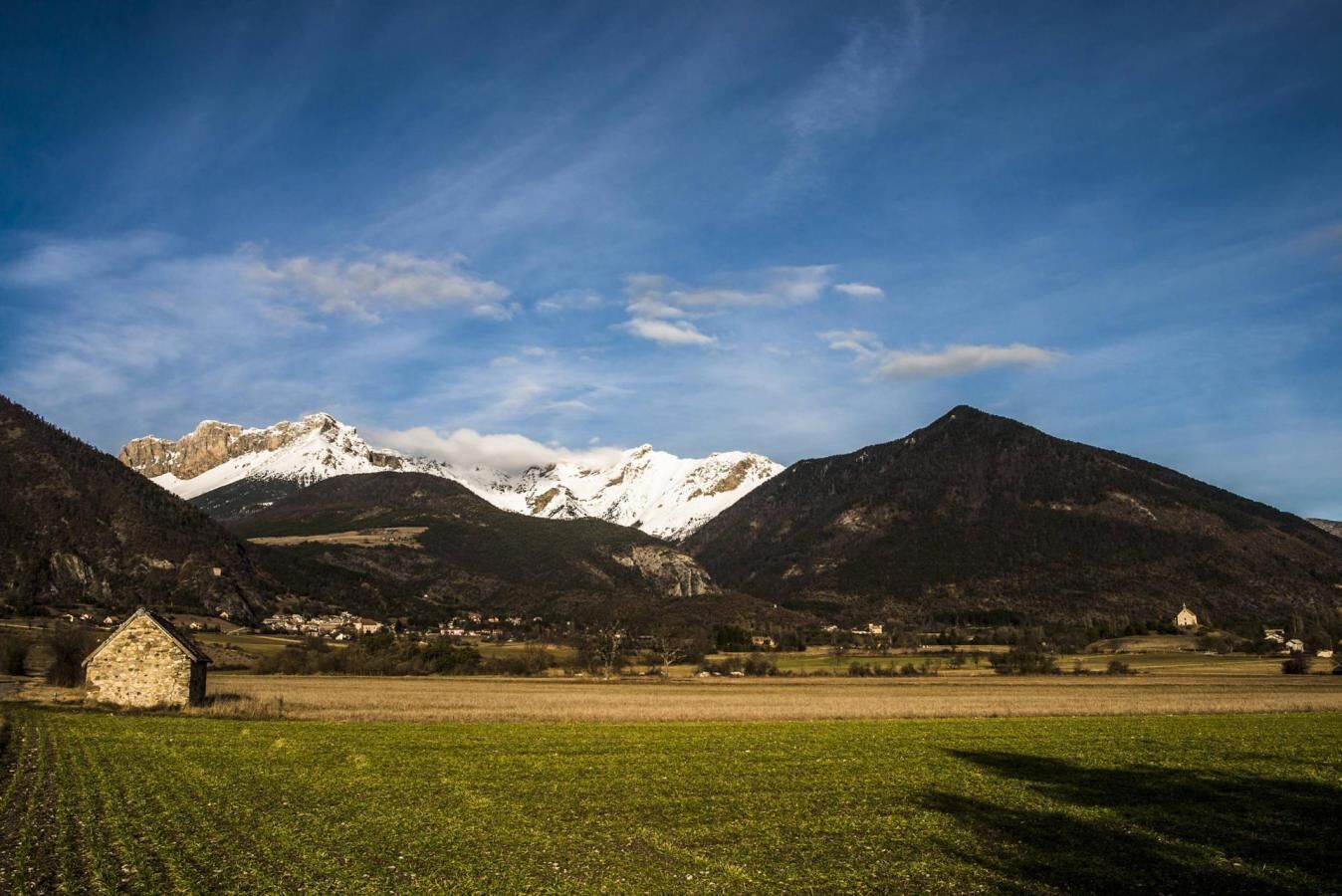 A rural landscape with mountains, a small stone building, and open fields.