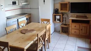 Een kleine keuken met een eettafel, stoelen, een koelkast, een magnetron, een koffiezetapparaat, een klok en een televisie.