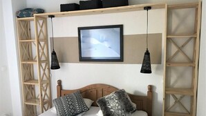 Een slaapkamer met een houten hoofdbord, twee kussens, een witte deken, een ingelijst beeld aan de muur en twee hangende lampen.
