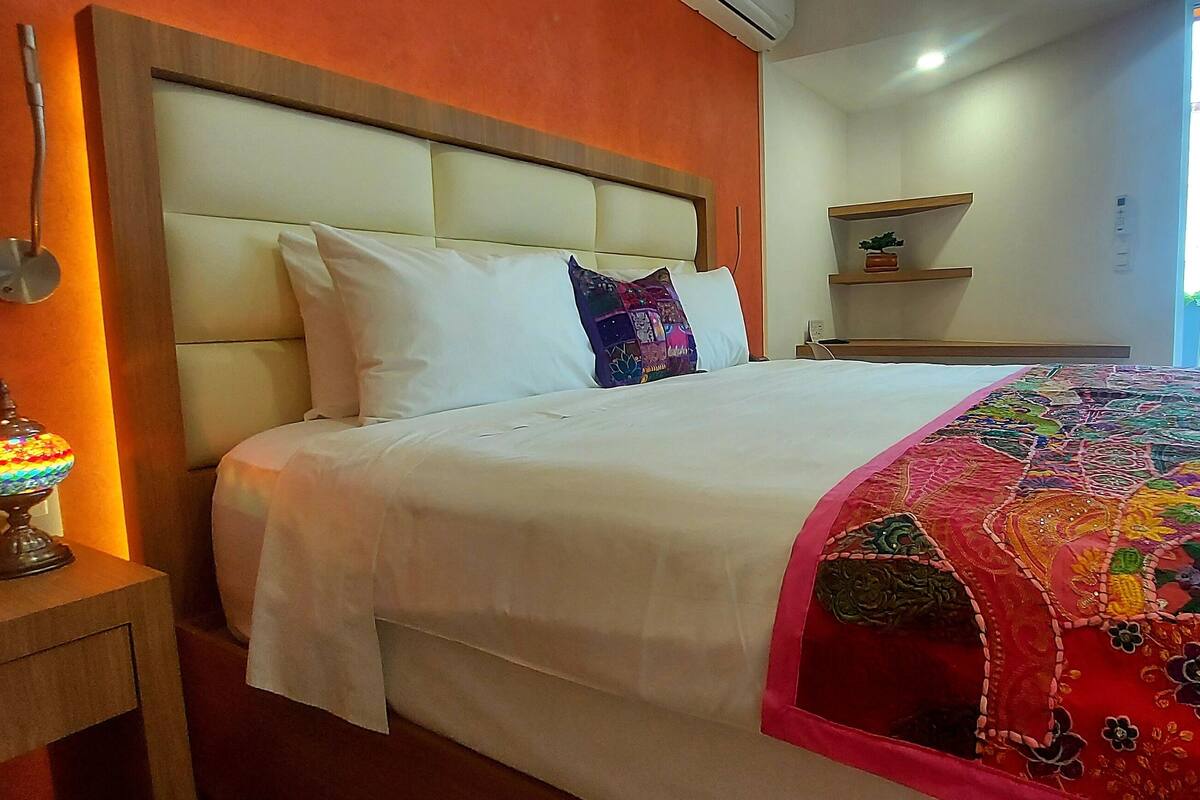 Een hotelkamer met een bed, nachtkastje, lamp en raam met gordijnen.
