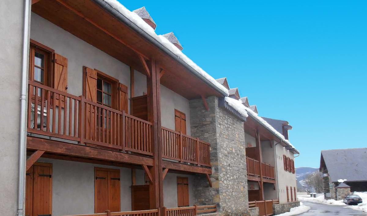 Un edificio in stile chalet tradizionale con balconi in legno e pilastri in pietra, con un cielo azzurro e terreno innevato.