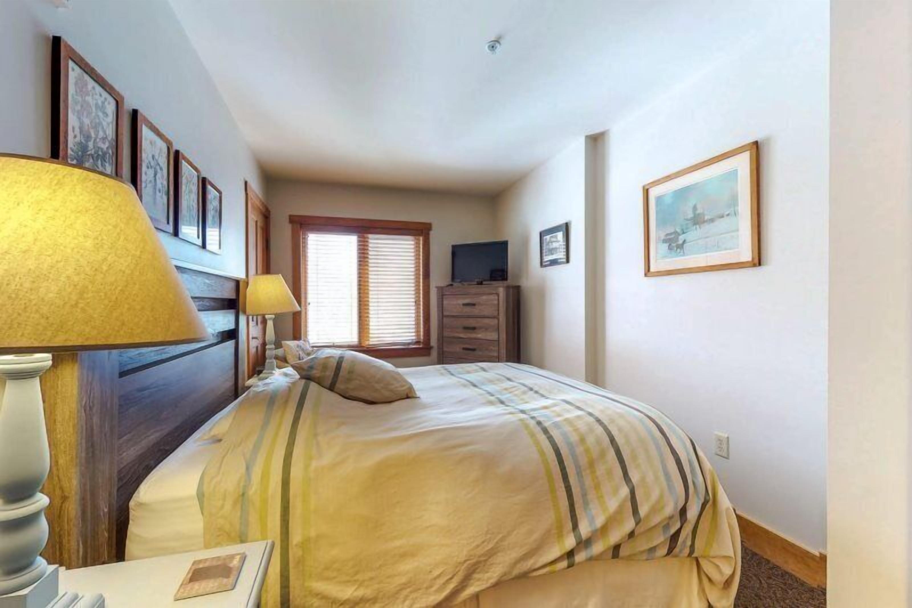 A bedroom with a bed, bedside lamps, a dresser, and framed pictures on the walls.