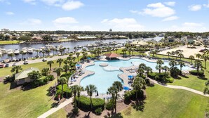 A resort with a large, irregularly shaped swimming pool surrounded by palm trees and lounge chairs. - North Tower #802 Spacious with Pool Views! (North Myrtle Beach)