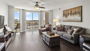 A spacious living room with a large window, a ceiling fan, and a view of a cityscape. - North Tower #802 Spacious with Pool Views! (North Myrtle Beach)