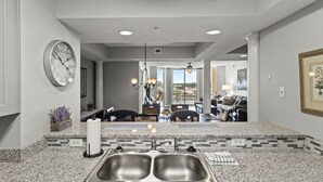 A kitchen with granite countertops, stainless steel sinks, and a visible clock. - North Tower #802 Spacious with Pool Views! (North Myrtle Beach)