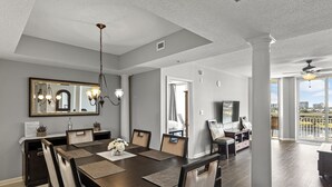 A spacious dining area with a long table, chairs, and a chandelier. There is a large mirror above the table and a television in the adjacent room. - North Tower #802 Spacious with Pool Views! (North Myrtle Beach)