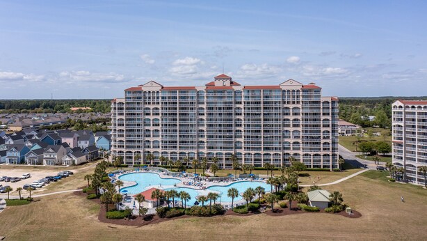 A large hotel with multiple floors, a central swimming pool, and surrounding greenery. - North Tower #802 Spacious with Pool Views! (North Myrtle Beach)