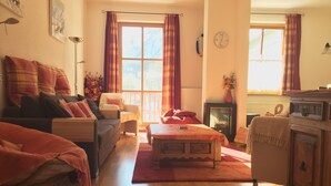 A cozy living room with a sofa, armchair, and a small table. There is a fireplace and a window with curtains. - Kitz Residenz 6, Kaprun, Zell am See, Salzburg (Kaprun)