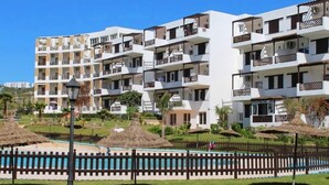 A multi-story hotel with balconies, a swimming pool, and a well-maintained garden. - Studio in Mirador Golf 4119 (Cabo Negro)